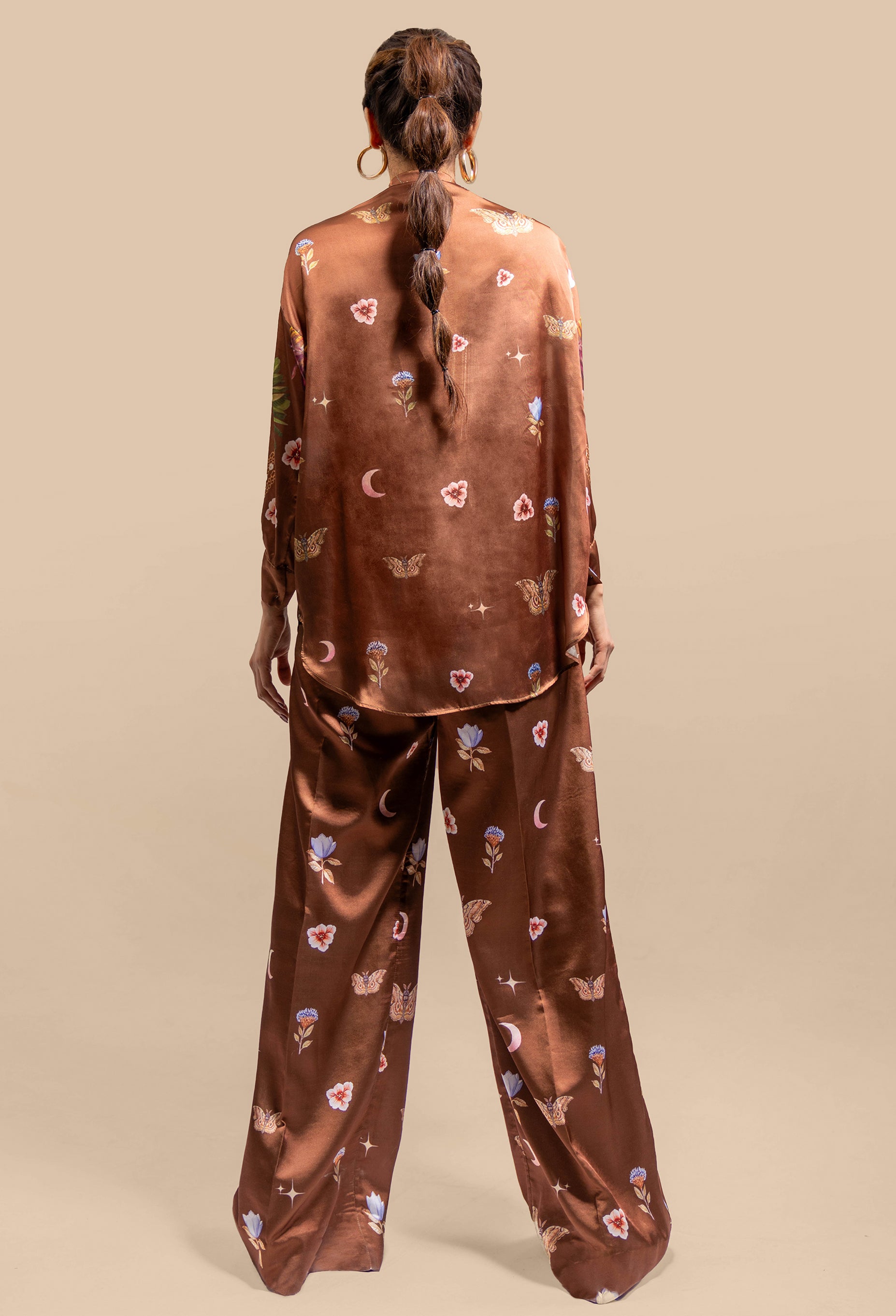 A back view of the Cosmic Print Silk Co-Ord Set, showcasing the blouse's relaxed drape and the wide-leg trousers. The high collar of the blouse and the fluidity of the silk create an elegant, flowing look from behind. The cosmic print continues seamlessly, wrapping around the entire set in a harmonious, celestial design.