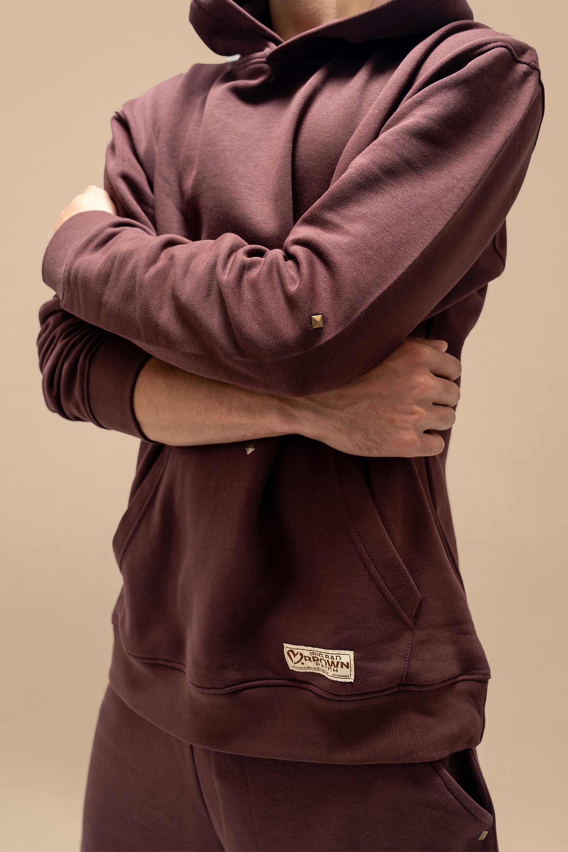 A close-up of the Chestnut Hoodie, highlighting its soft, plush fabric and relaxed silhouette. The hoodie features a drawstring at the neck, a front kangaroo pocket, and a subtle embroidered logo on the chest, adding a touch of simple detail to its laid-back design.

