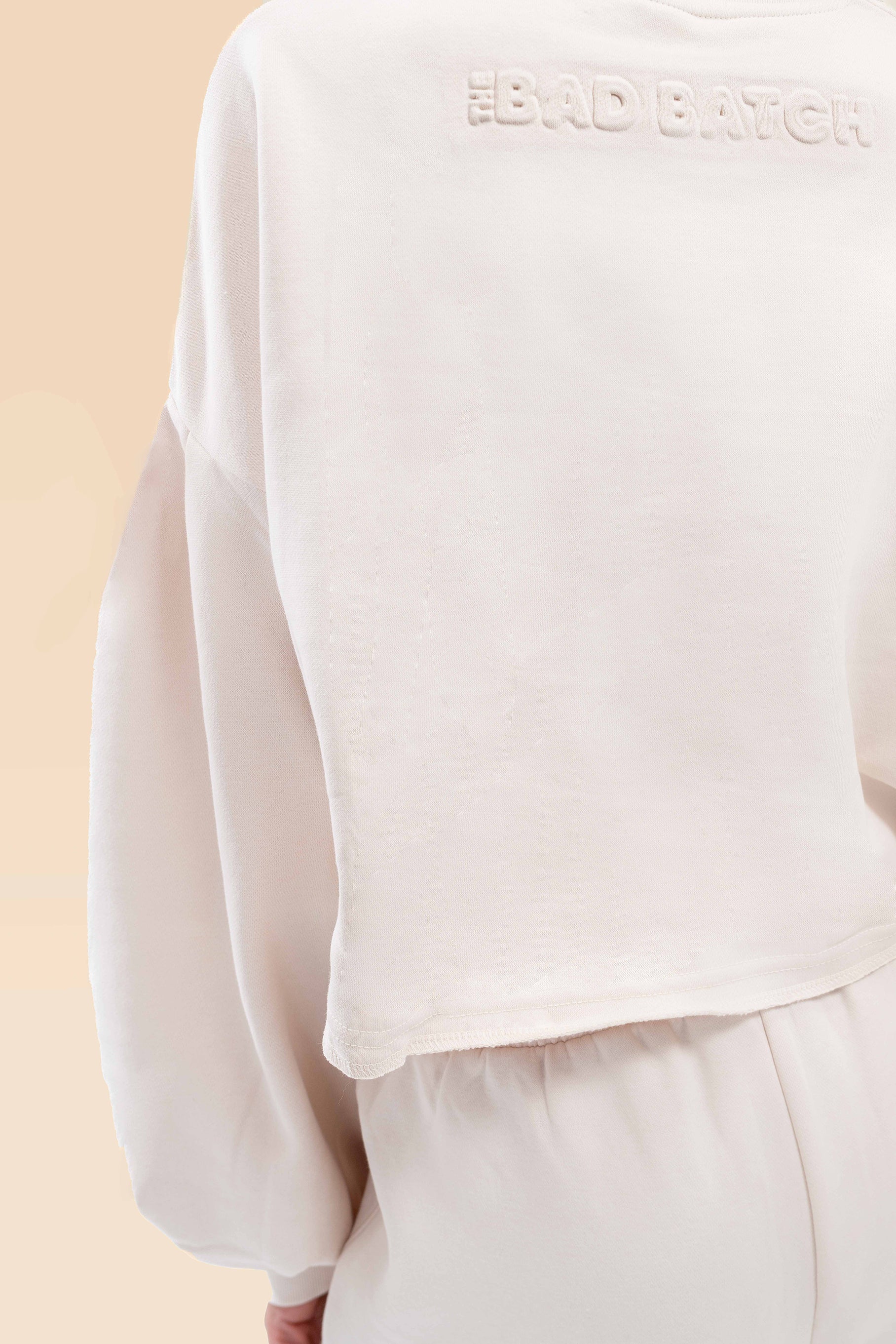 Detailed view of the high-waist pants, showcasing the smooth cream fabric and tailored fit.